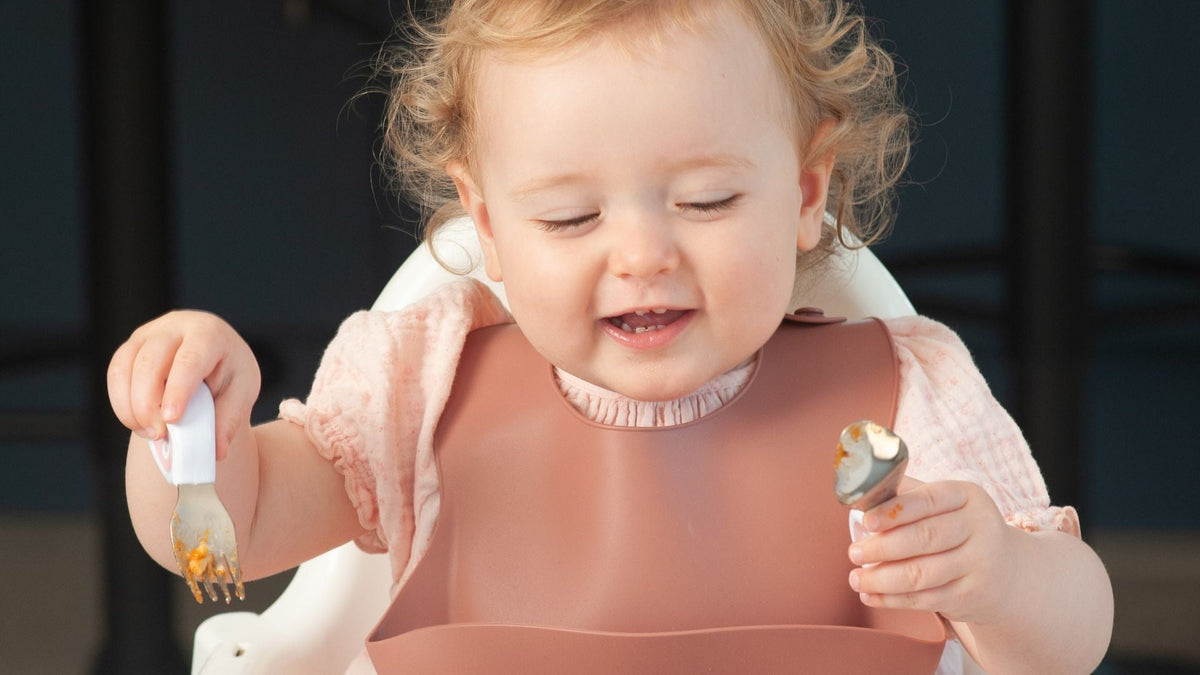 happy toddler girl holding toddler cutlery in both hands
