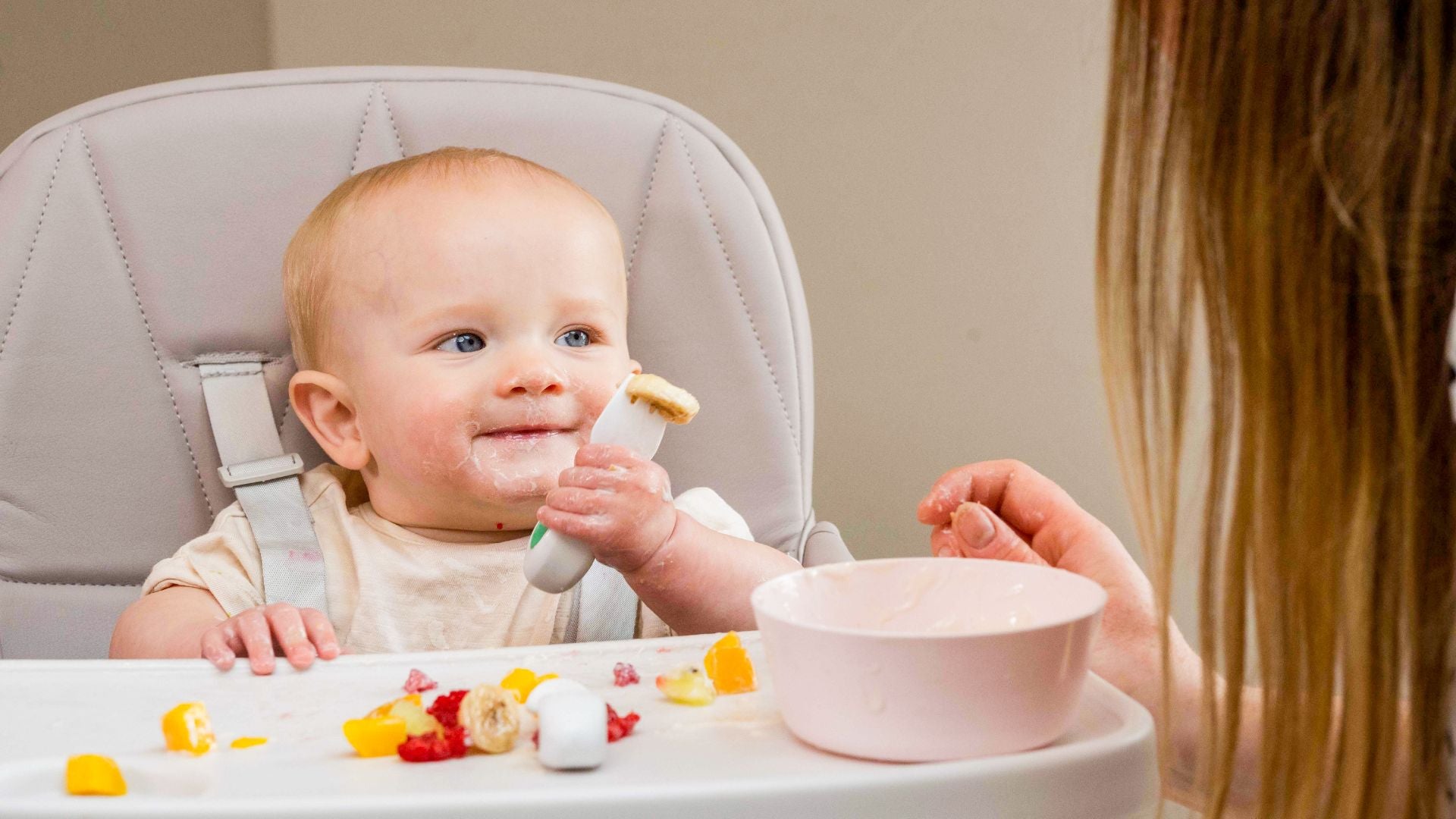 : Baby at highchair with first foods, mess on face, happy expression