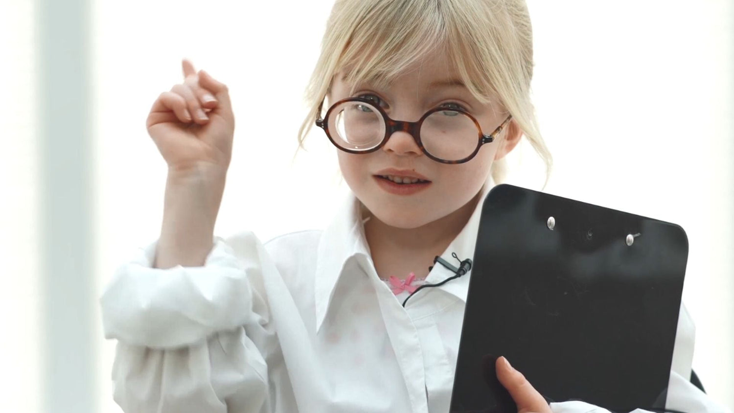 toddler girl dressed as a scientist with glasses and clipboard, she is holding one finger in the air