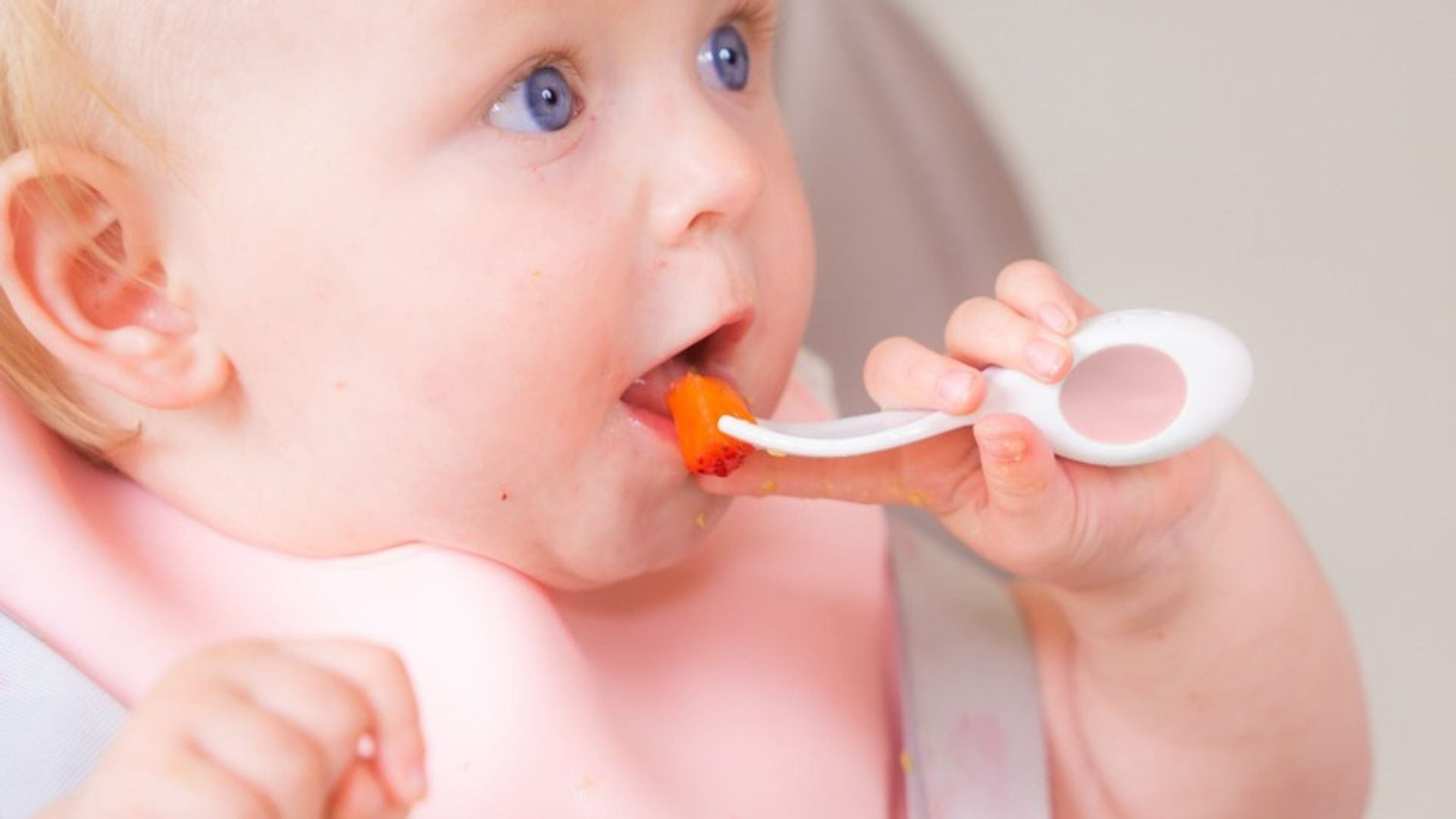 Baby girl happily using a doddl baby spoon to feed herself a piece of fruit