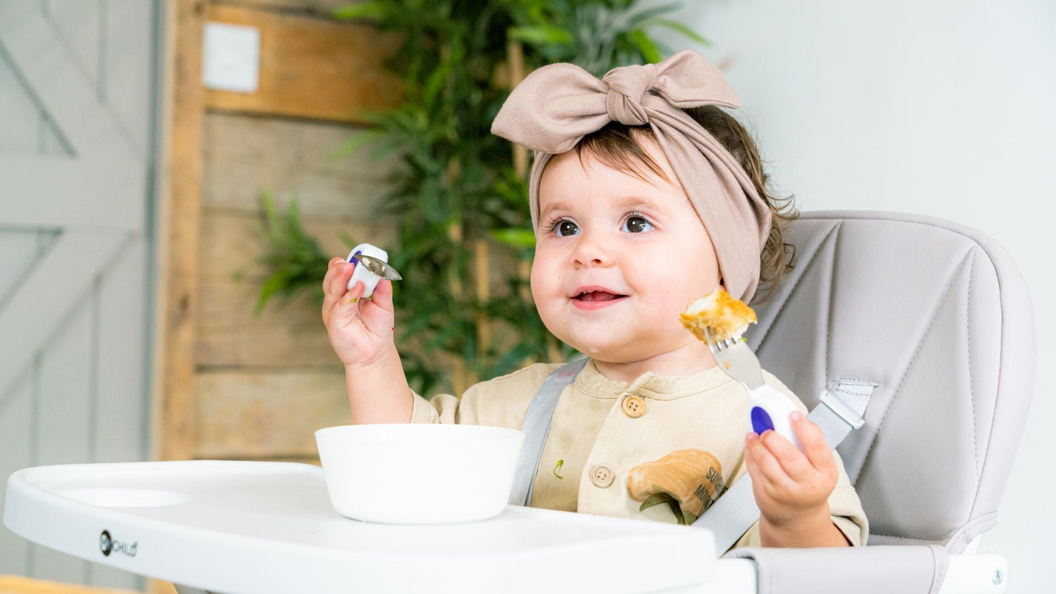 Happy contented toddler sitting in a high chair with toddler cutlery and bowl