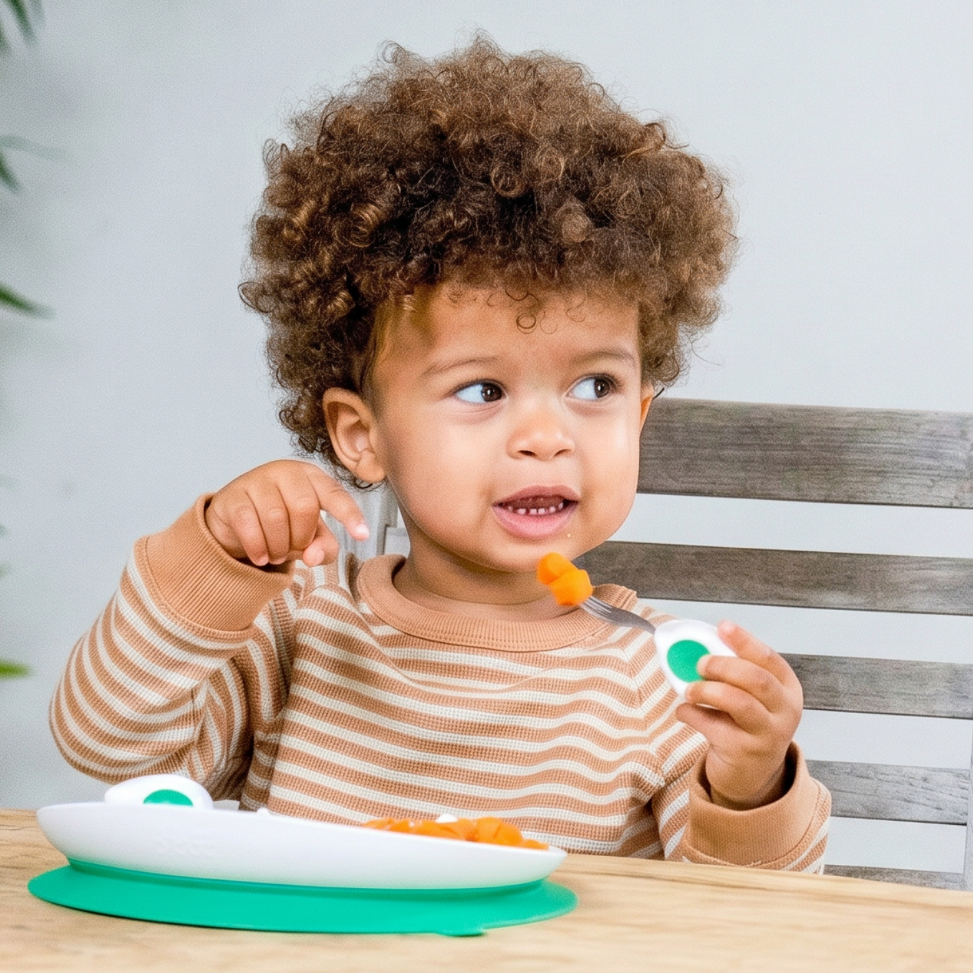 Child sitting at a table with a plate of food, holding doddl utensils.