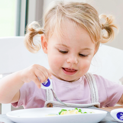 Child eating with a doddl fork in a bright kitchen