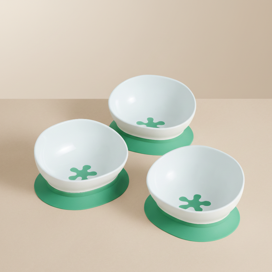 Three white doddl bowls with green bases on a beige background