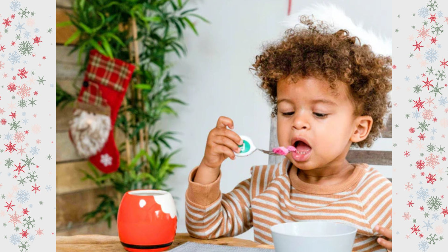 Toddler wearing Christmas hat eating with doddl toddler cutlery