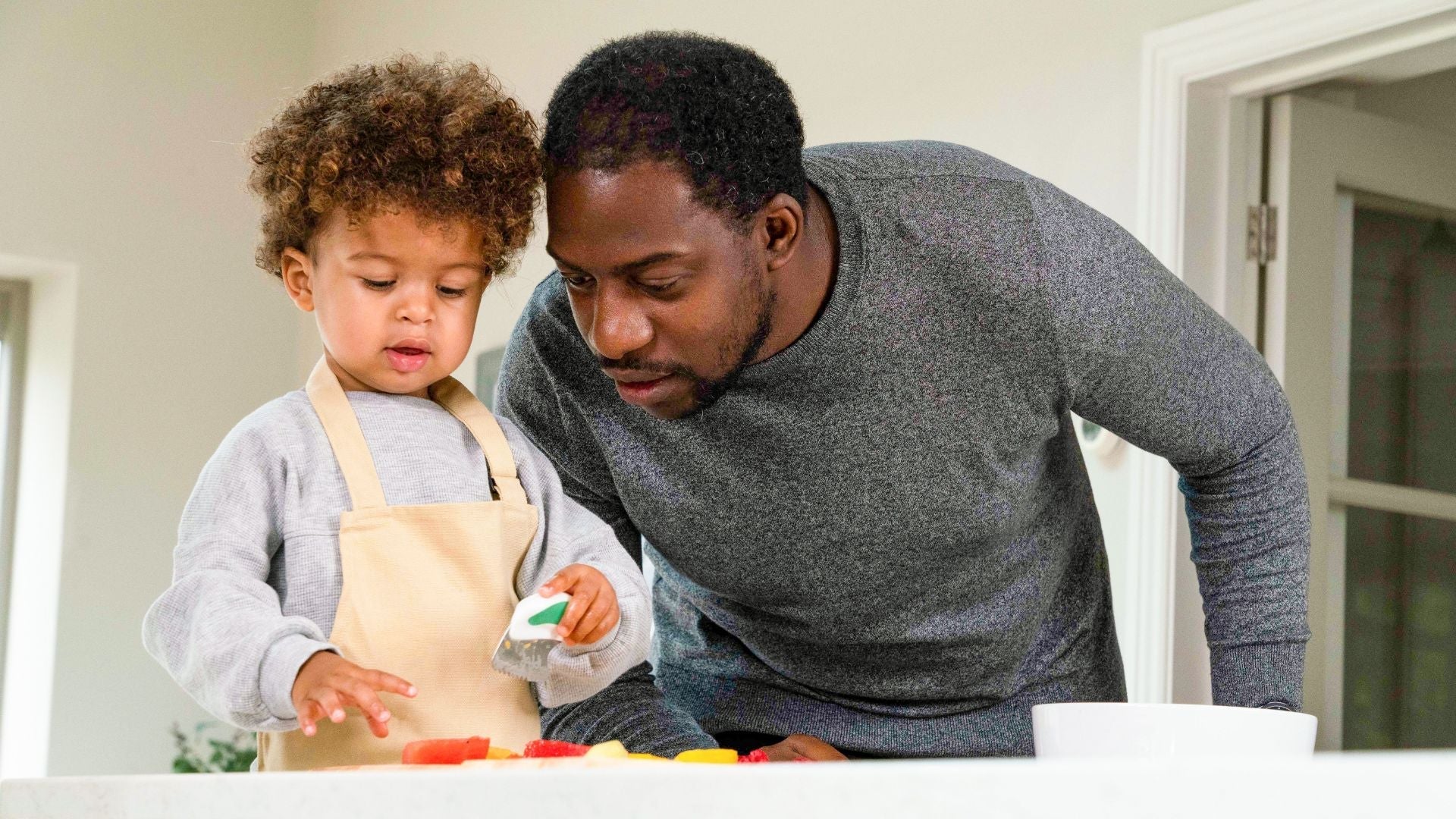 Father and son together, focusing on the toddler boy cutting food with his toddler-safe doddl knife