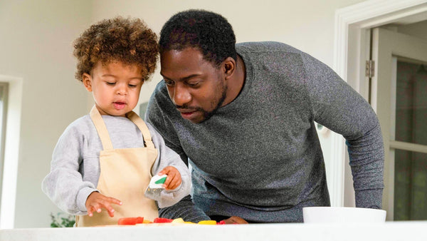 Father and son together, focusing on the toddler boy cutting food with his toddler-safe doddl knife