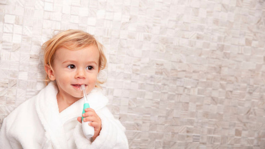 toddler boy in a white dressing gown holding a BabySonic electric toothbrush