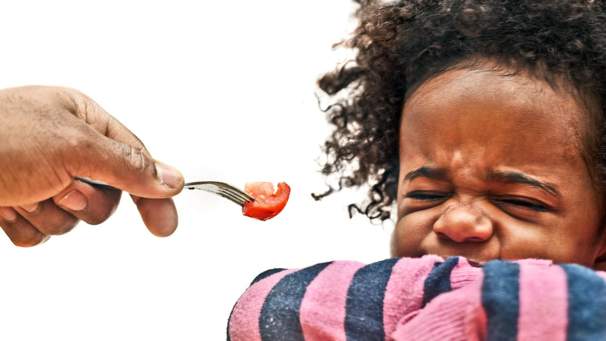 toddler screwing up face and hiding mouth when offered a piece of tomato held out on a fork
