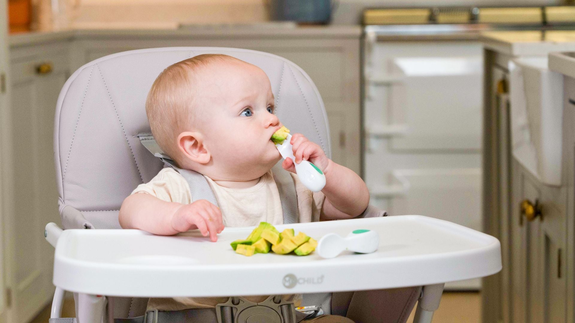 Baby boy in highchair learning to eat food with his doddl baby cutlery