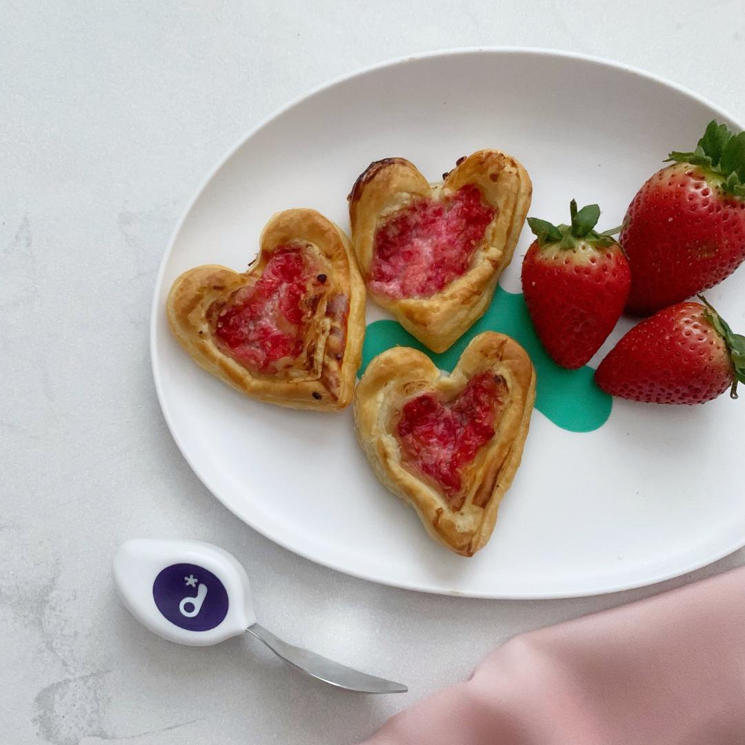 Raspberry Tarts - recipe from doddl. Heart shaped pastries with jam on a doddl plate with a doddl toddler knife|Raspberry Tarts - recipe from doddl doddl plate and fork with little hand