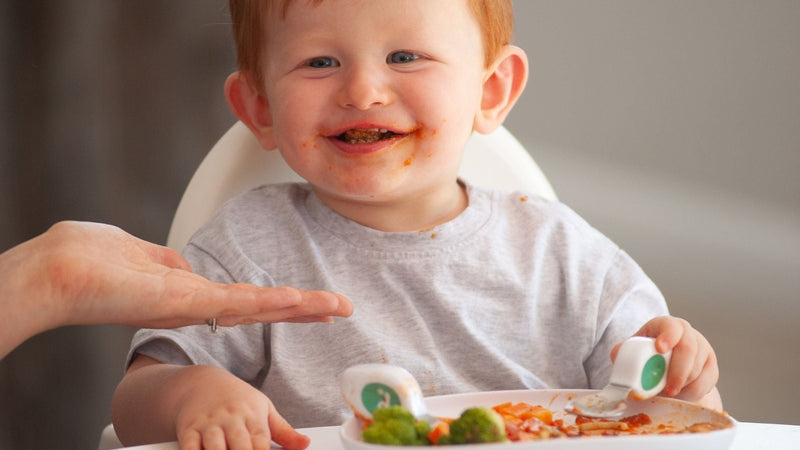 Happy toddler boy eating a meal with doddl toddler cutlery