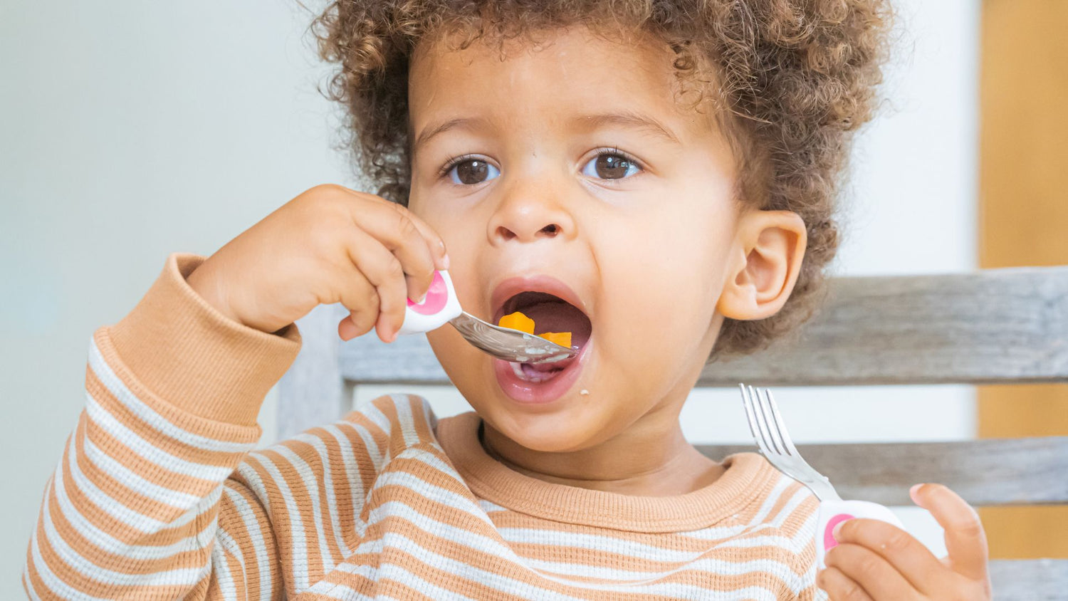 toddler boy using a doddl toddler spoon to eat independently