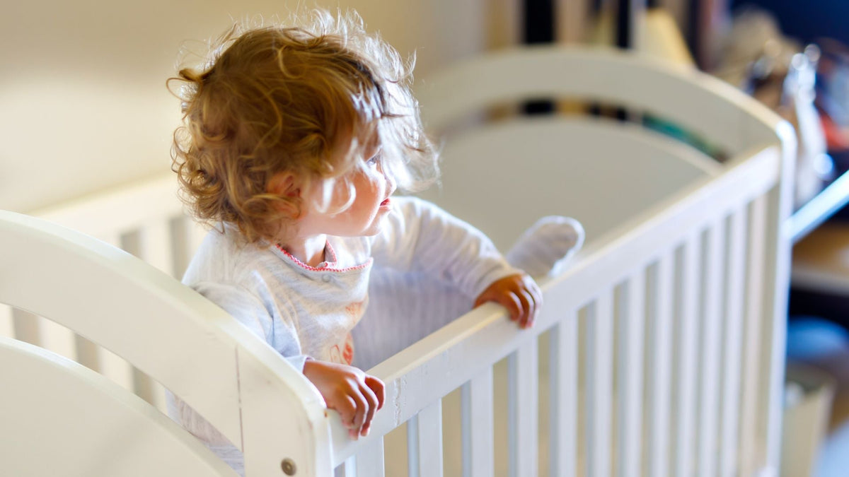 toddler in a white cot bed, one leg is lifted to try to climb out