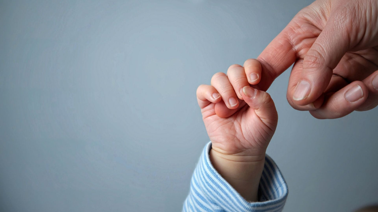 One month old baby gripping parent’s finger, close up of tiny hand