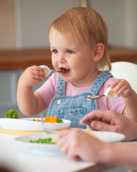 Toddler feeding themselves with doddl cutlery at the table