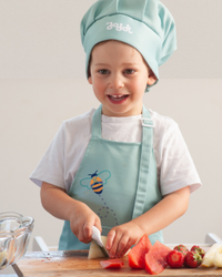 Smiling child in a chef's hat cutting fruit with a doddl toddler knife
