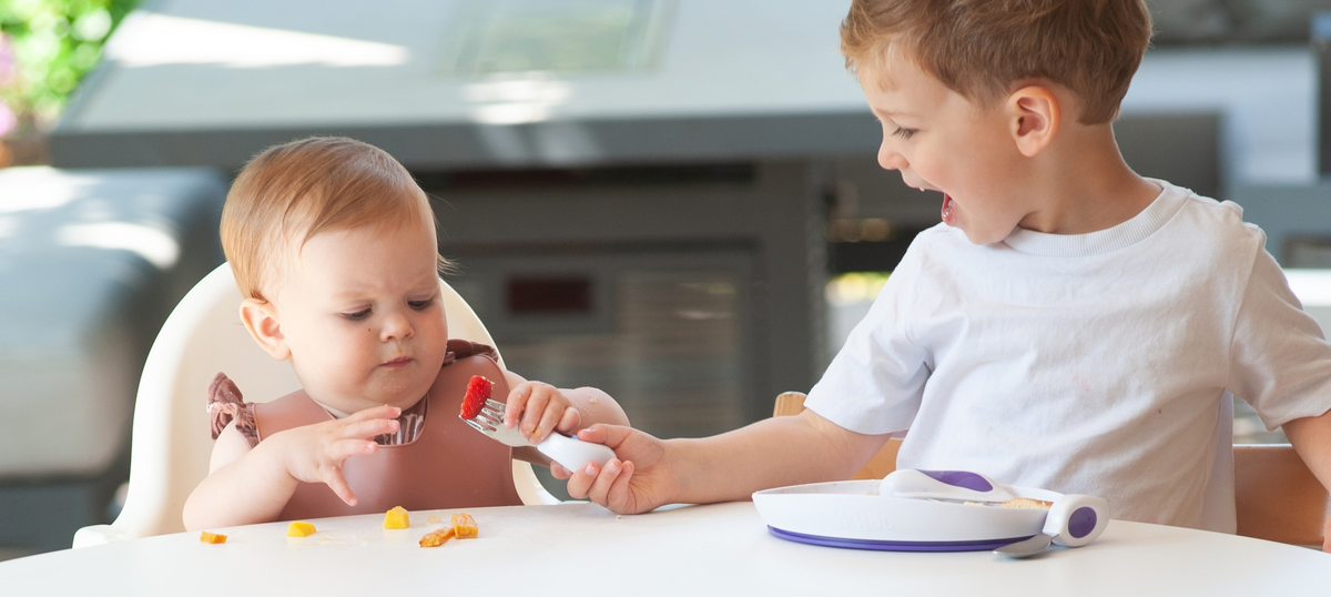 A family in the kitchen, toddler slicing a banana with a doddl knife