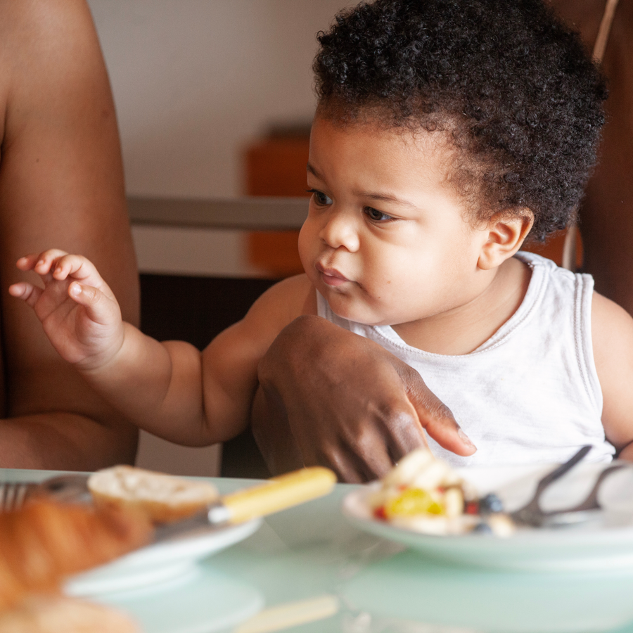 A baby at the table watching a parent eat