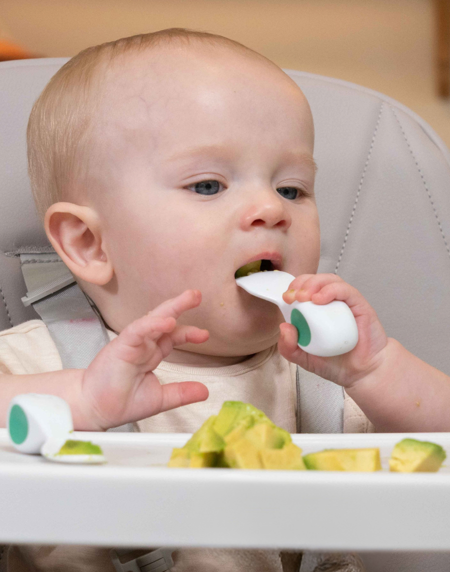 A baby holding a doddl spoon in a whole-fist grip