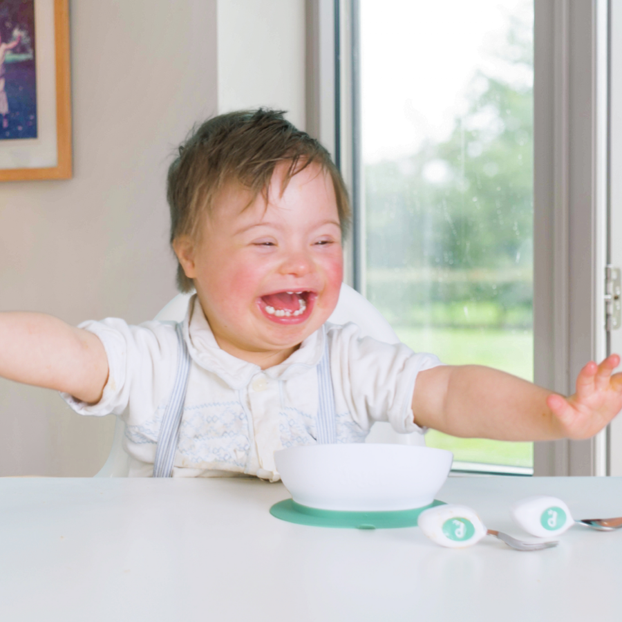 Laughing baby at the table with a doddl bowl and cutlery