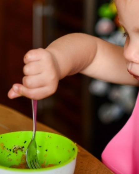 A toddler gripping a standard fork in a whole fist