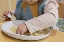 A child holding a doddl spoon in one hand while exploring food with the other