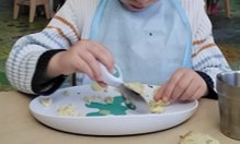 A child using a doddl spoon while their other hand steadies the food on the plate