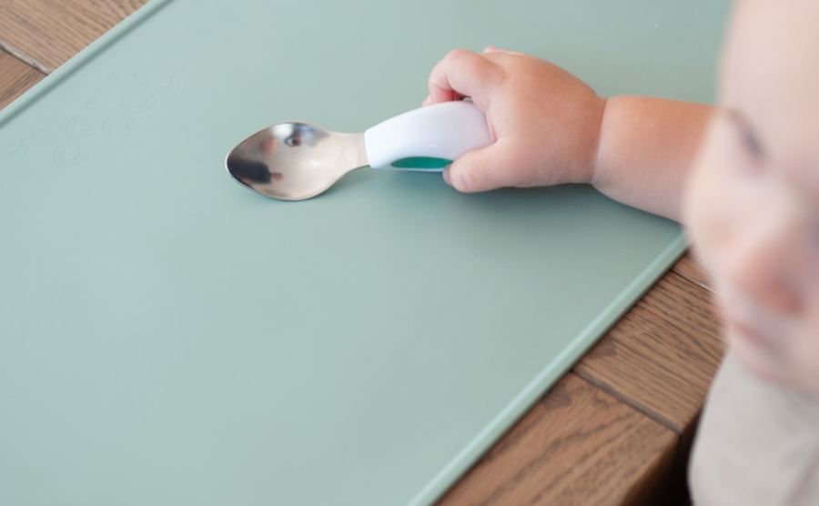 A baby holding a doddl spoon between thumb and fingers