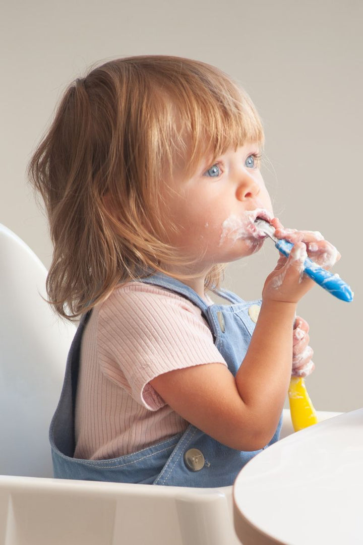 A toddler eating with a long-handled spoon, elbow raised