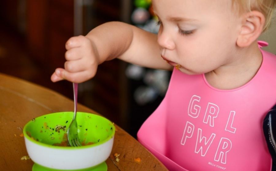A toddler gripping a standard fork in a whole fist